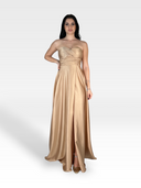 Una donna indossa un abito color champagne dorato lungo fino al pavimento LAKME del 18esimo secolo. L'abito incarna l'eleganza senza tempo, caratterizzato da un corpetto con ruches e una gonna fluida. Ha lunghi capelli scuri ed è in posa con una mano sul fianco su uno sfondo bianco.